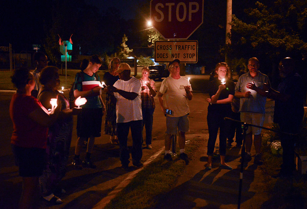 Attendees hold candles in front of the stop sign